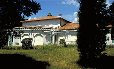 Villa présentant une pièce en rotonde précédée d'une rotonde précédée d'une terrasse délimitée par une barrière en bois comme la pergola.