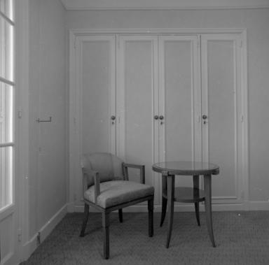 Vue de détail d'un fauteuil et d'un guéridon situés dans une chambre.