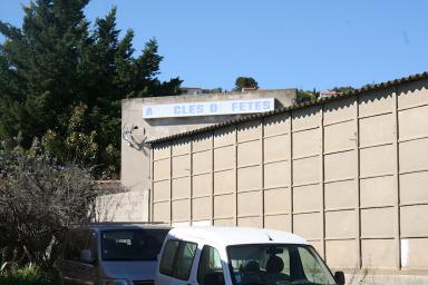 Vue sur la fin du bâtiment de type entrepôt au sud-ouest et sur un bâtiment en fond portant la signalétique de l'entreprise