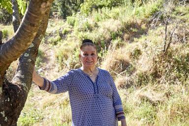 Madame Aldjia Sylvie Koulal, fille de Harki, devant un cerisier planté sur le terrain de l'ancien hameau où elle a vécu petite.