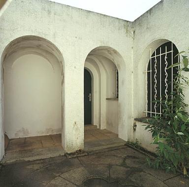 Le patio. Vue de volume prise de l'ouest vers la porte d'entrée du cottage.