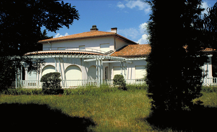 Villa prsentant une pice en rotonde prcde d'une rotonde prcde d'une terrasse dlimite par une barrire en bois comme la pergola.